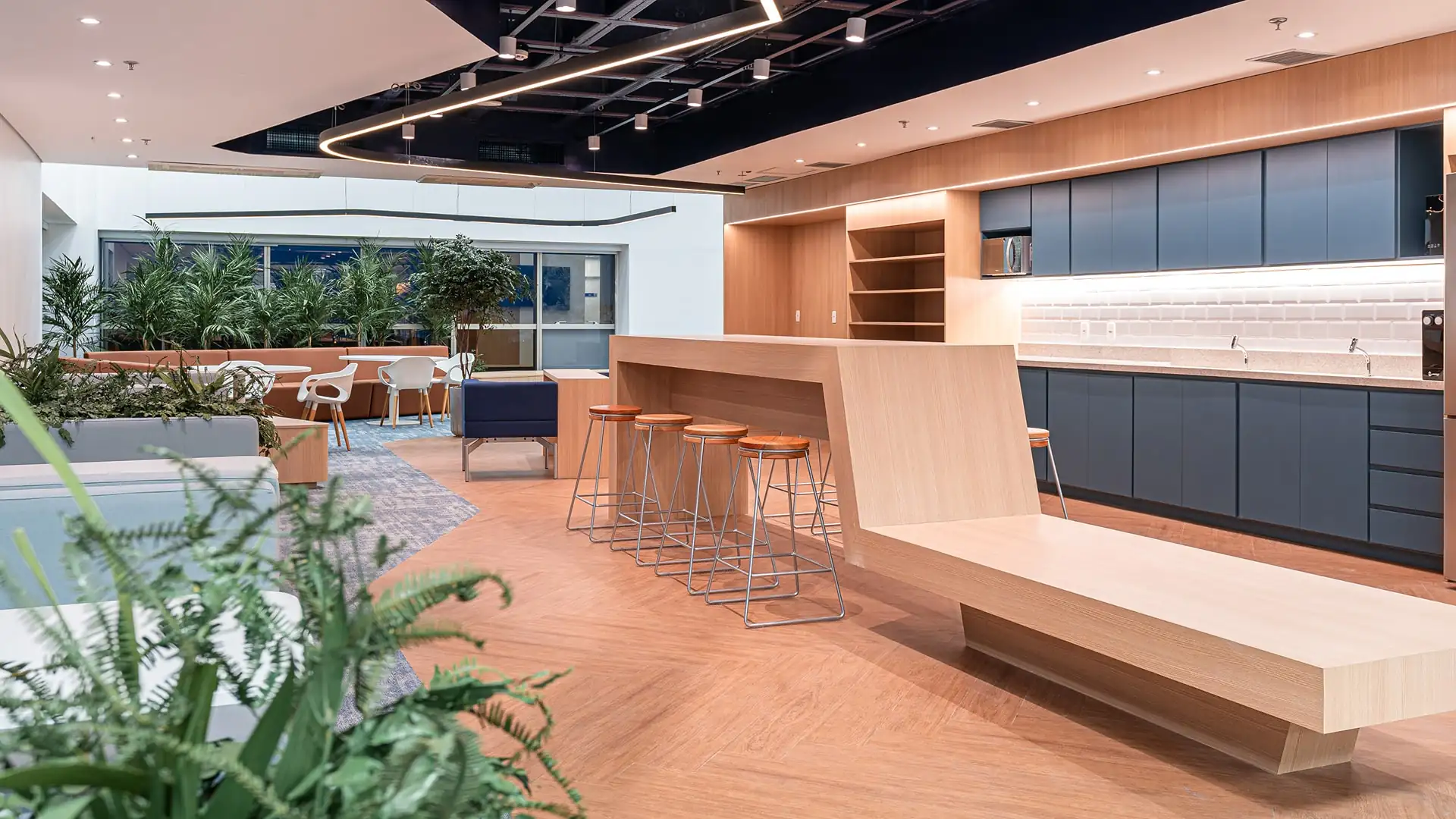Área de convivência corporativa do escritório da Oceaneering com bancada de madeira, cozinha moderna e mobiliário contemporâneo, valorizando projeto de arquitetura e reforma de escritório executados pela Custódio.