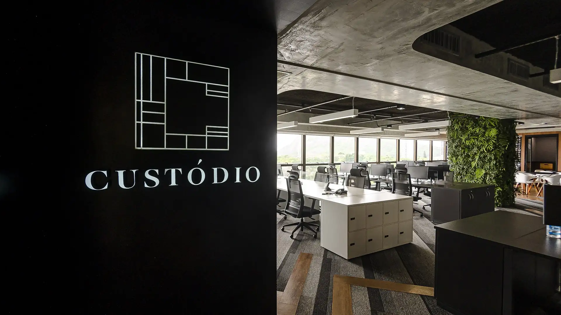 Recepção e open space do escritório da Custódio com design corporativo moderno, painel verde, estações de trabalho e acabamento industrial sofisticado, destacando projeto de arquitetura e reforma de escritório de alto padrão.