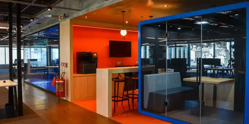 Área do escritório da EDF com espaço de trabalho informal com parede laranja e mobiliário moderno, destacando projeto de arquitetura realizado por escritório de arquitetura em uma obra corporativa funcional.