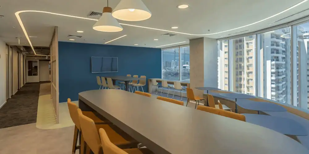 Área de convivência do escritório da Huawei com mesas altas, cadeiras amarelas, parede azul e janelas amplas, resultado de um projeto de arquitetura integrado a uma obra corporativa moderna e a uma reforma de escritório funcional.