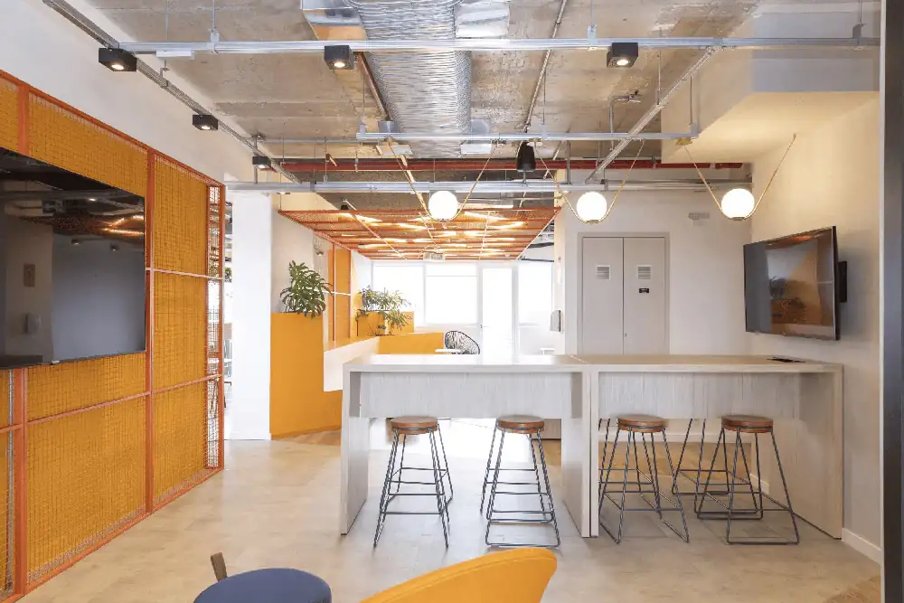 Área de convivência do escritório da Lalamove com mesas altas, bancos industriais e divisórias laranja, destacando o projeto de arquitetura aplicado na obra corporativa e na reforma de escritório com atmosfera moderna.