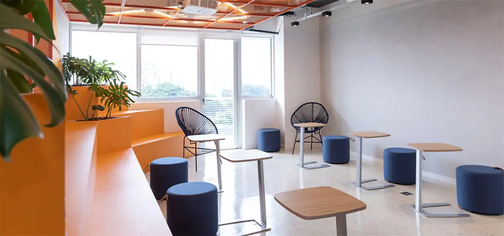 Área de descompressão da Lalamove com arquibancada laranja, bancos azuis e mesas individuais, destacando o projeto de arquitetura da obra corporativa e a reforma de escritório com estética moderna e funcional.