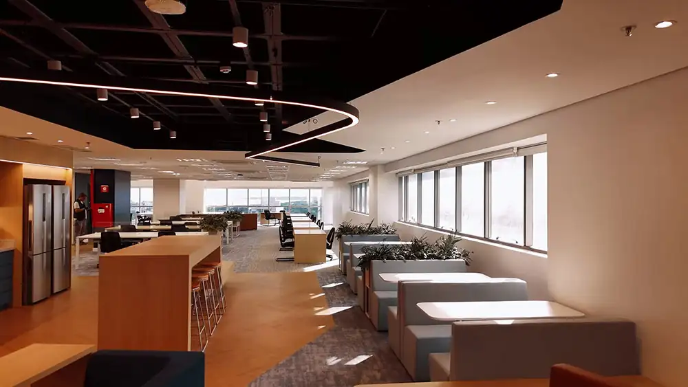 Área de convivência e staff da Oceaneering no Rio de Janeiro, projeto de arquitetura e obra corporativa pela Custódio. Espaço corporativo amplo com cabines, mesas colaborativas e iluminação moderna, integrando conforto, funcionalidade e design no ambiente de trabalho.