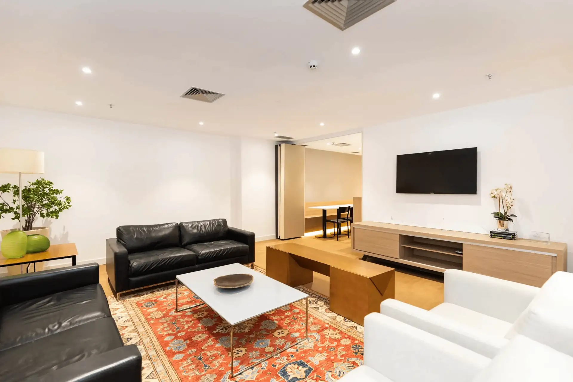 Área de descanso da ATG com sofás, poltronas claras, tapete decorativo e rack de madeira, representando um projeto de arquitetura acolhedor dentro de uma obra corporativa e de uma reforma de escritório moderna.