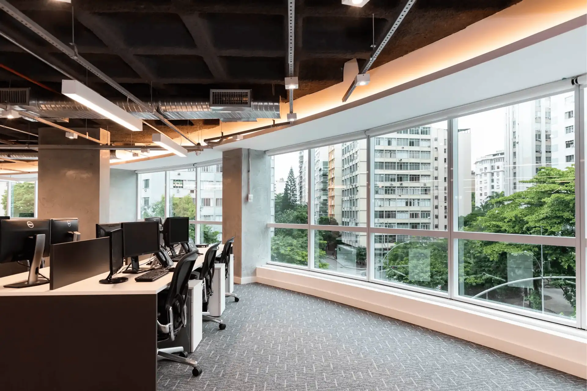 Open office da ATG com janelas panorâmicas, estações alinhadas e teto industrial, destacando um projeto de arquitetura corporativa integrado a uma obra corporativa moderna e à reforma de escritório com iluminação eficiente.