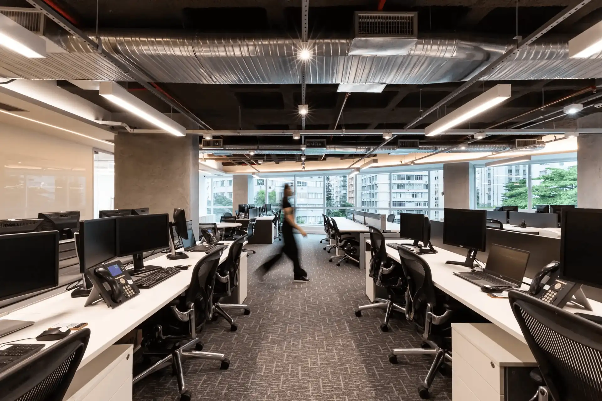 Open office da ATG com estações de trabalho alinhadas, iluminação industrial e ampla vista urbana, mostrando um projeto de arquitetura funcional integrado a uma obra corporativa e a uma reforma de escritório moderna.