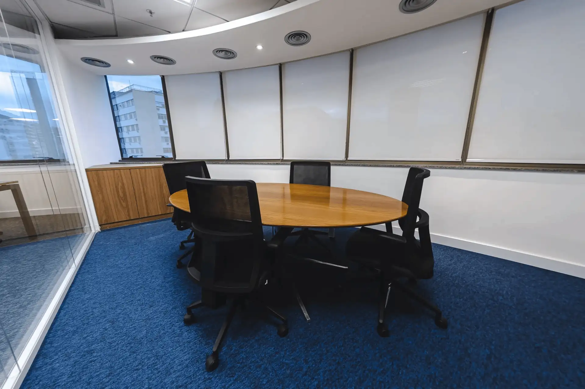 Sala de reunião do escritório da ATG com mesa oval de madeira, cadeiras pretas e carpet azul, mostrando soluções de projeto de arquitetura aplicadas em obra corporativa e reforma de escritório.