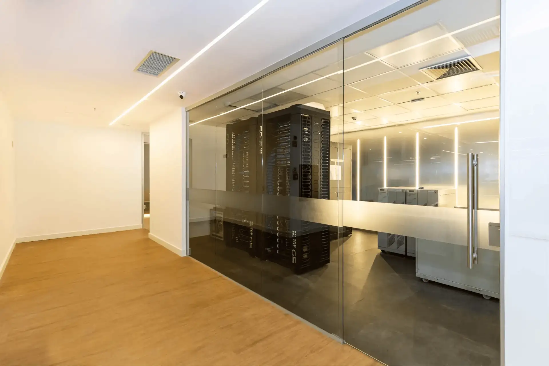 Sala de servidores da ATG com racks de TI vistos por vidro, iluminação técnica e piso elevado, mostrando como o projeto de arquitetura, a obra corporativa e a reforma de escritório garantem infraestrutura moderna e segura.