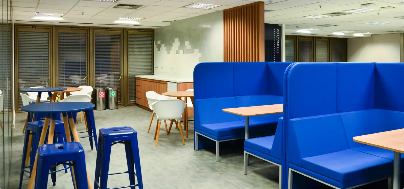 Área de convivência da Brother com booths azuis, mesas altas e cadeiras brancas, destacando projeto de arquitetura moderno, obra corporativa funcional e reforma de escritório voltada ao conforto dos colaboradores.
