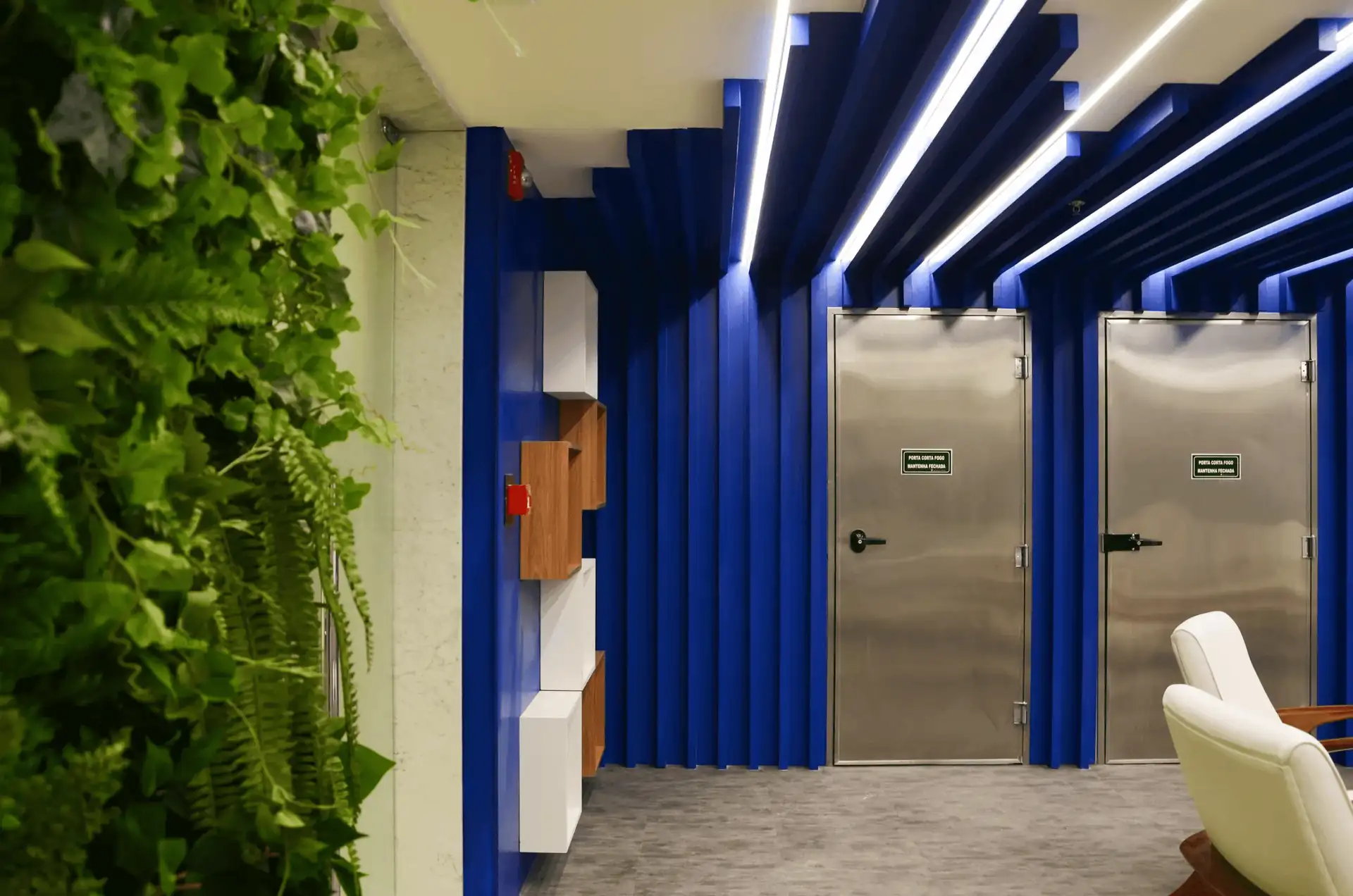 Hall de acesso da Brother com parede azul estruturada, portas metálicas, jardim vertical e nichos decorativos, evidenciando projeto de arquitetura detalhado, obra corporativa moderna e reforma de escritório sofisticada.