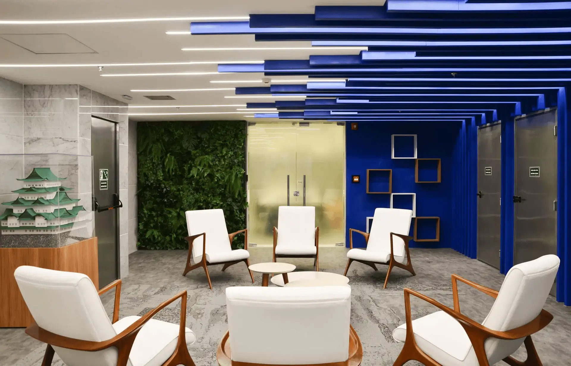 Recepção corporativa da Brother com poltronas brancas, parede verde natural e teto azul geométrico, destacando projeto de arquitetura moderno, obra corporativa detalhada e reforma de escritório com identidade visual marcante.