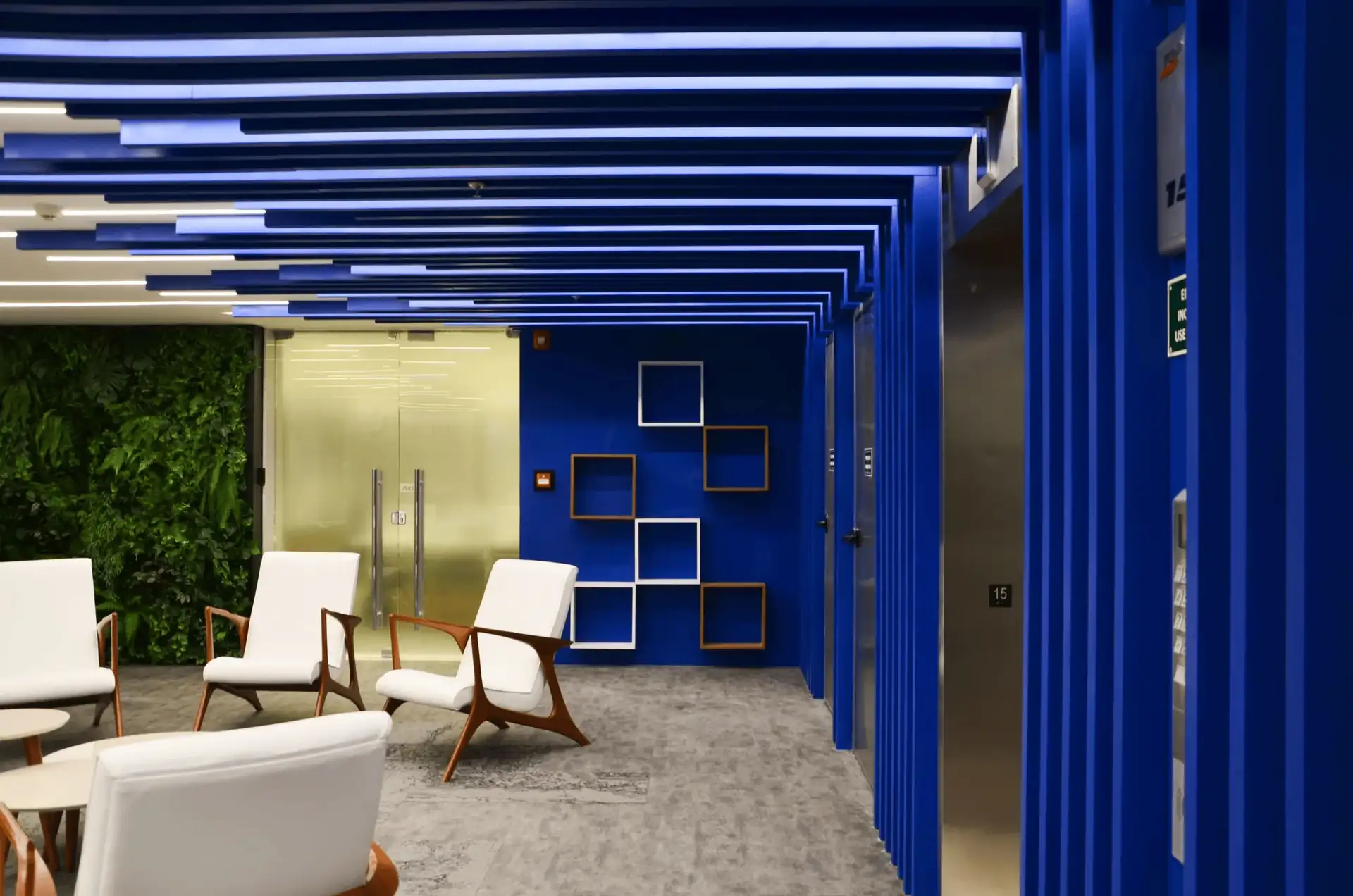 Recepção corporativa da Brother com teto azul geométrico, poltronas brancas e parede verde, destacando projeto de arquitetura moderno, obra corporativa refinada e reforma de escritório focada em identidade visual.