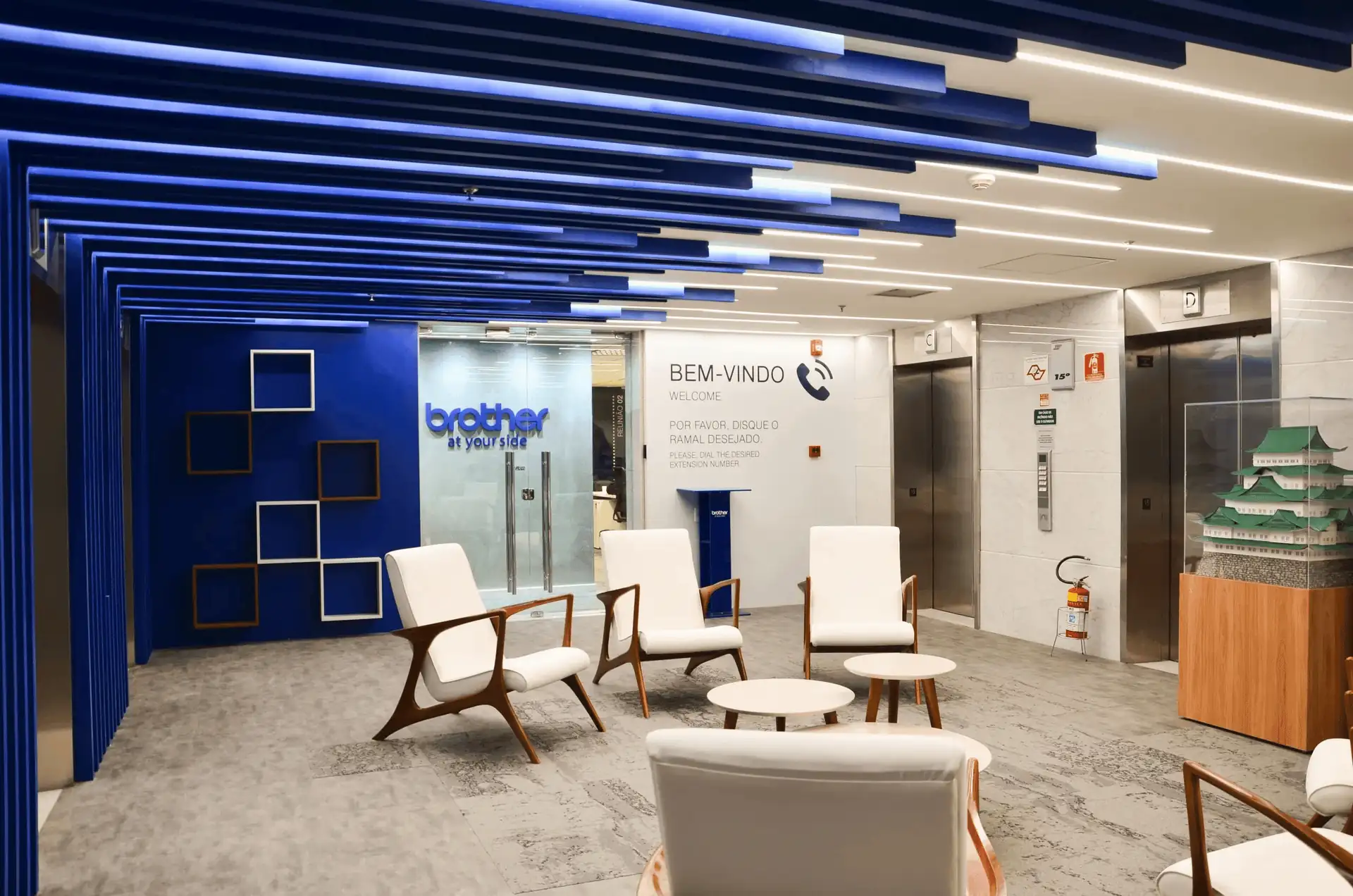 Recepção corporativa da Brother com poltronas brancas, teto azul escultural e paredes modernas, destacando projeto de arquitetura sofisticado, obra corporativa completa e reforma de escritório voltada à identidade da marca.