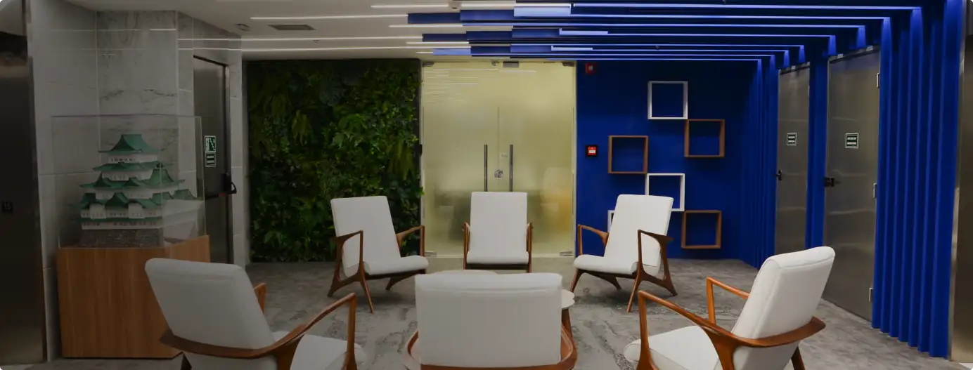 Recepção da Brother com poltronas brancas, jardim vertical, teto azul geométrico e nichos decorativos, destacando projeto de arquitetura cuidadoso, obra corporativa completa e reforma de escritório moderna.