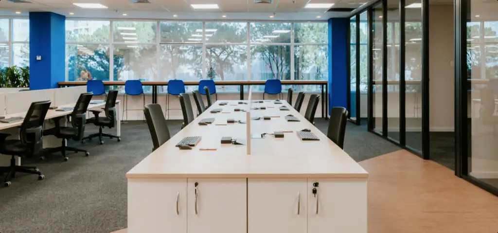 Open space do escritório da Vestas com estações de trabalho organizadas, cores corporativas em azul e preto e divisórias envidraçadas, destacando projeto de arquitetura corporativa e reforma de escritório moderna e funcional.