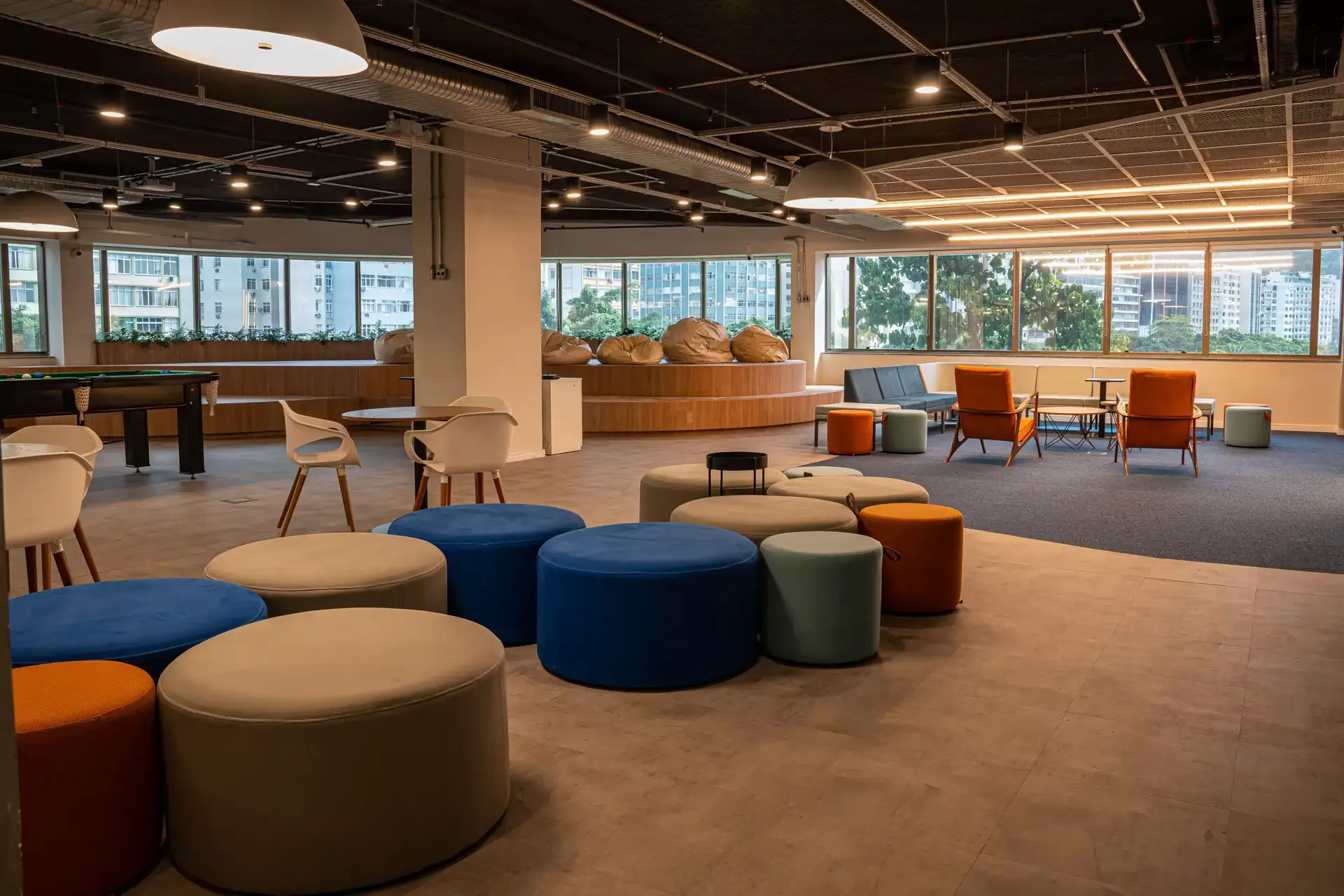 Área de convivência do escritório da Eneva projetada pela Custódio, com puffs coloridos, poltronas, mesas de apoio, mesa de sinuca e iluminação industrial. Espaço amplo, acolhedor e flexível para descanso e integração dos colaboradores.