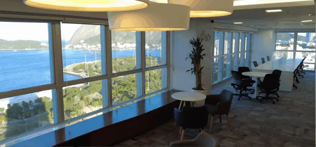 Escritório da NTS no Rio de Janeiro com ampla vista para o mar, mesas de trabalho e área de convivência moderna. Ambiente planejado por escritório de arquitetura, integrando projeto de arquitetura, obra corporativa e reforma de escritório com foco em conforto, iluminação natural e produtividade.