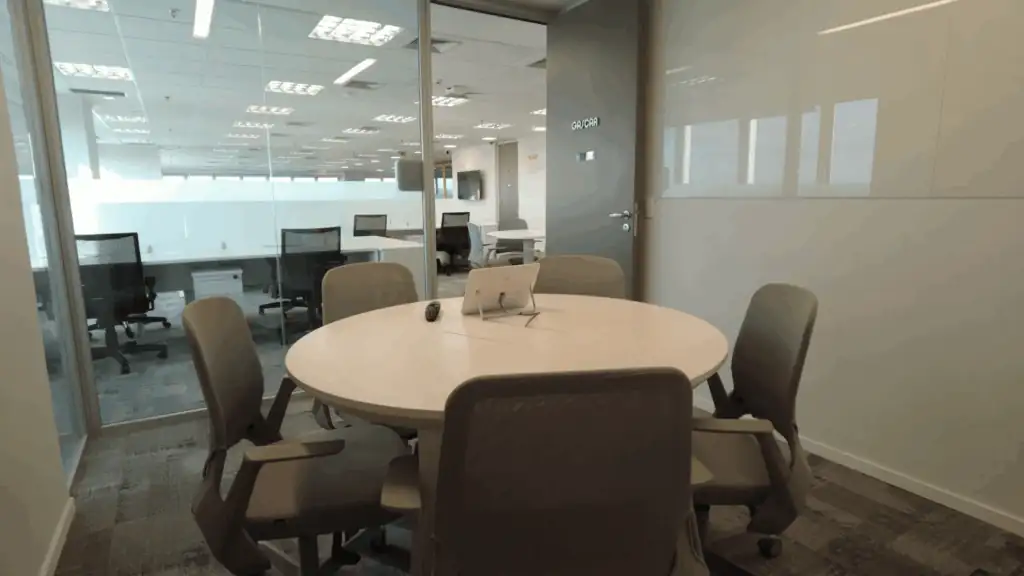Sala de reunião do escritório da NTS com mesa redonda, cadeiras ergonômicas e divisórias de vidro, demonstrando um ambiente funcional criado por escritório de arquitetura. O espaço reflete um projeto de arquitetura corporativa, resultado de uma obra corporativa completa e reforma de escritório que prioriza privacidade, conforto e eficiência para reuniões e alinhamentos.