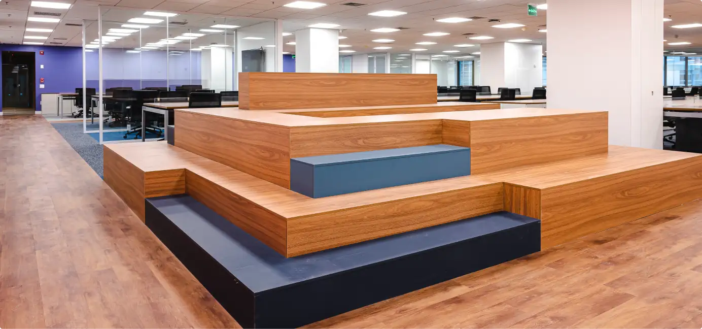 Escada-arquibancada em madeira no escritório do Parque Bondinho, integrada ao open space e destacando o projeto de arquitetura, a obra corporativa completa e a reforma de escritório com foco em convivência e funcionalidade.