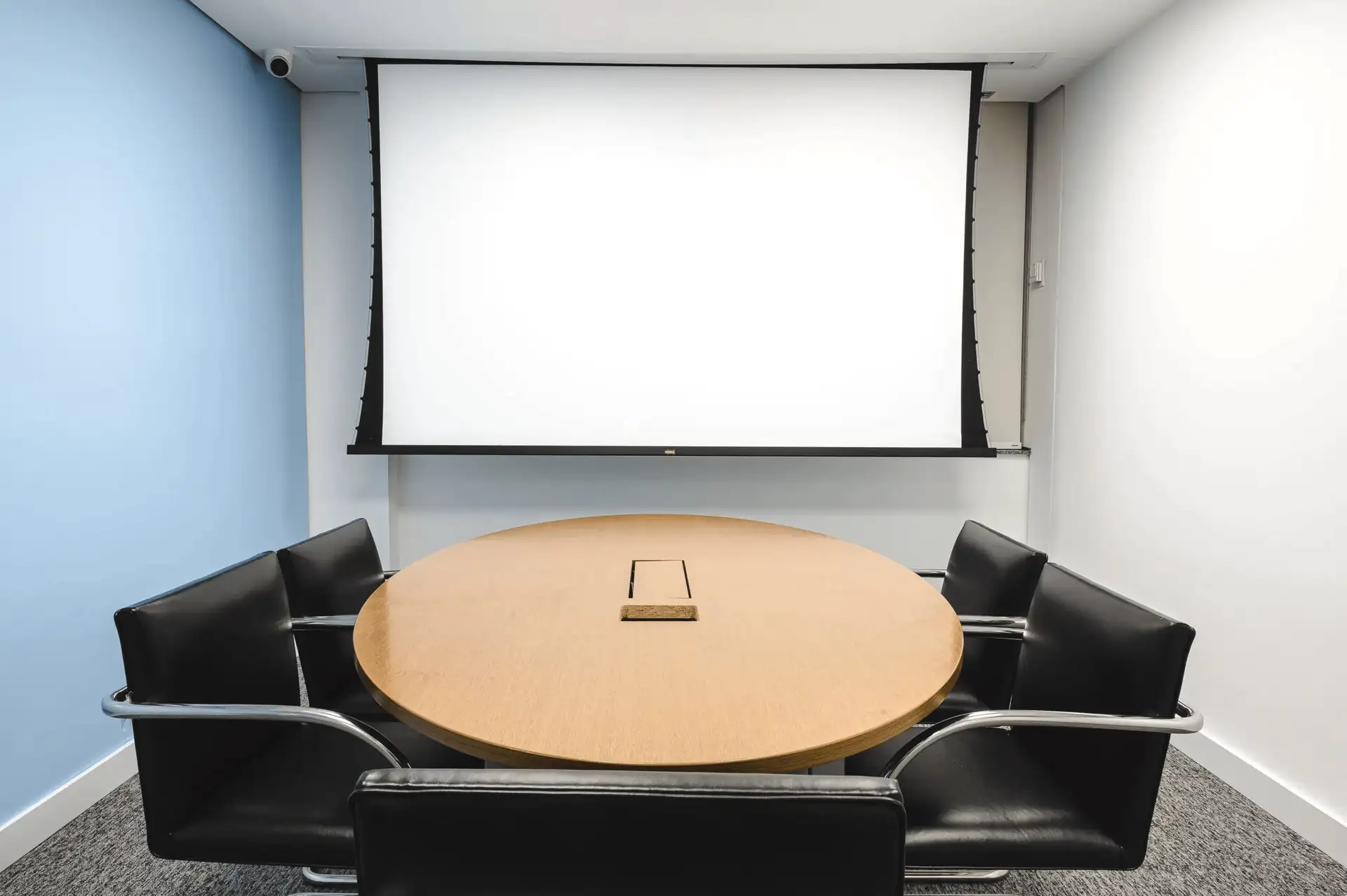 Sala de reunião do escritório do Parque Bondinho com mesa redonda de madeira, cadeiras pretas e tela de projeção, destacando solução de projeto de arquitetura aplicada em obra corporativa e reforma de escritório.