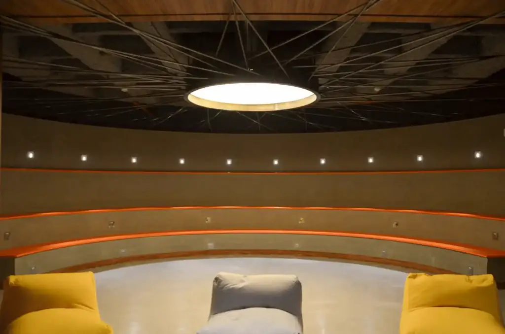 Auditório circular projetado por escritório de arquitetura, com arquibancadas curvas, iluminação central e acabamento moderno. Projeto de arquitetura integrado a uma obra corporativa e reforma de escritório de alto padrão.