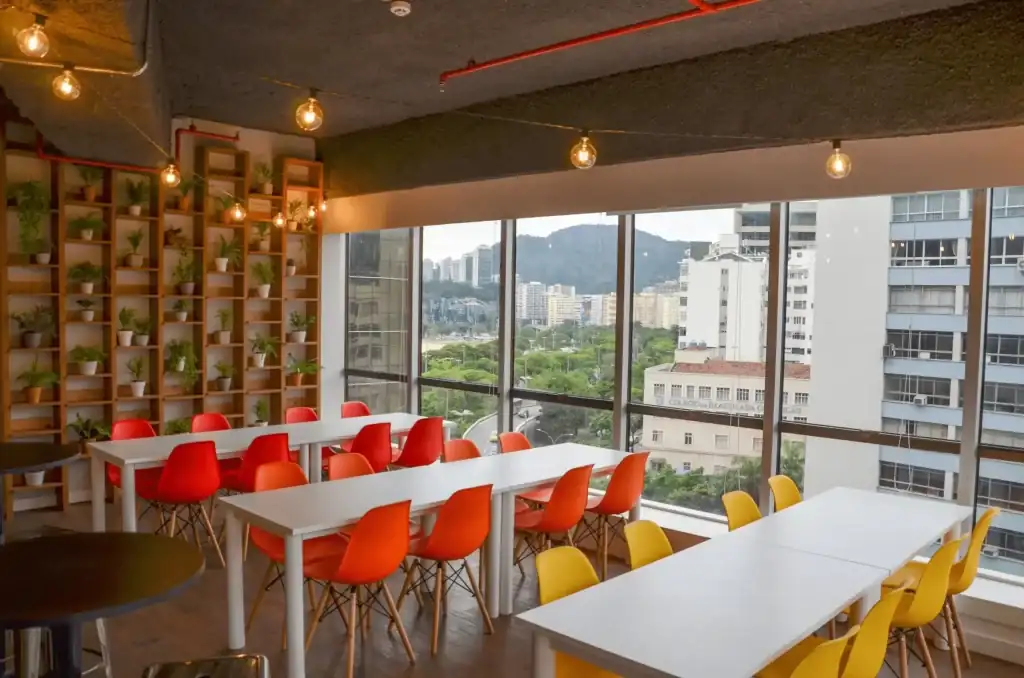 Refeitório moderno da Passei Direto com mesas brancas, cadeiras coloridas e parede verde, desenvolvido por escritório de arquitetura. Projeto de arquitetura voltado para obra corporativa e reforma de escritório, com vista panorâmica da cidade.