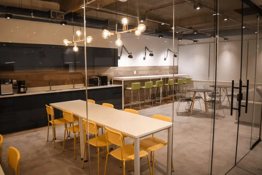 Área de convivência do escritório da Pebmed com mesas coletivas e bancadas altas, mostrando um ambiente moderno desenvolvido em projeto de arquitetura e reforma de escritório corporativo.