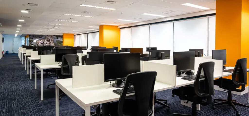 Open space do escritório da Saipem com estações de trabalho modernas, divisórias brancas e pilares amarelos, representando um projeto de arquitetura focado em eficiência e reforma de escritório corporativa.