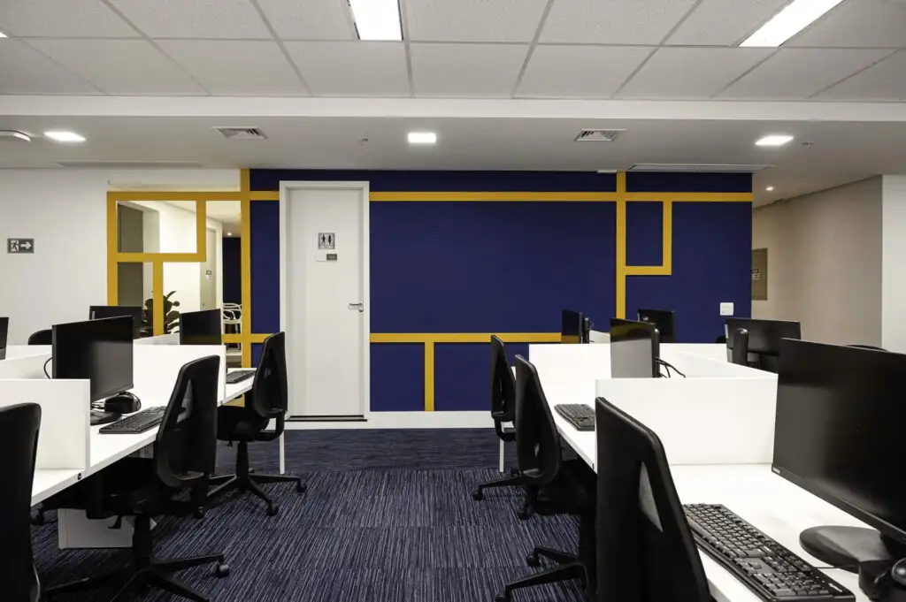 Open space do escritório da Saipem com estação de trabalho corporativa e parede azul com detalhes amarelos, destacando projeto de arquitetura e reforma de escritório com identidade visual moderna.