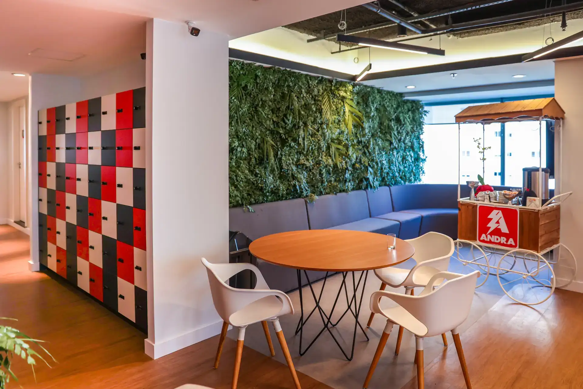 Área de convivência da Andra com lockers coloridos, mesa de apoio e parede verde, resultado de projeto de arquitetura e reforma de escritório finalizada em obra corporativa.