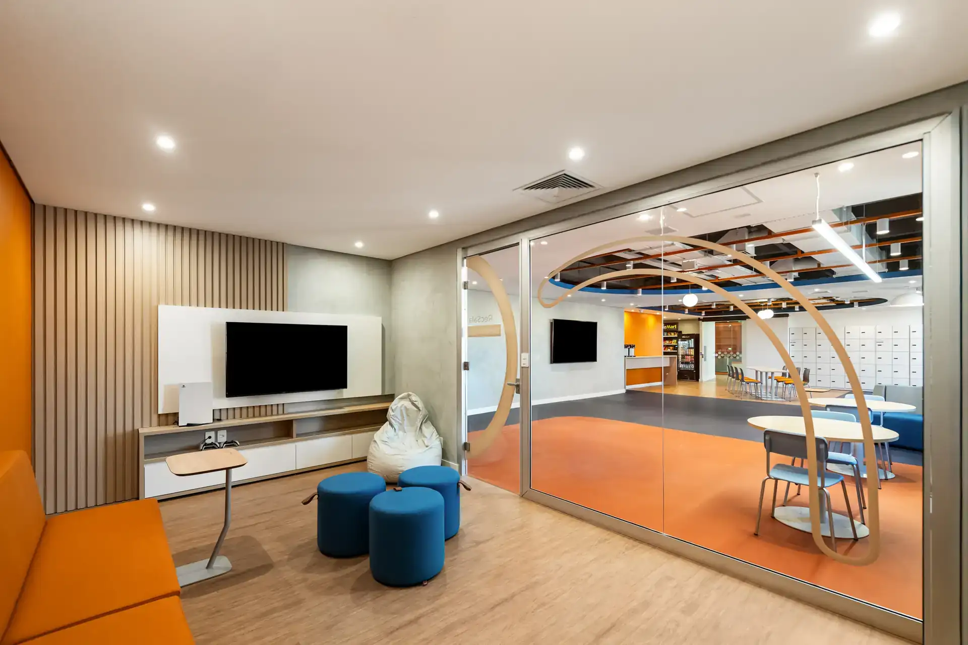 Sala de descanso criada por projeto de arquitetura corporativa com sofá, puffs e integração visual para áreas de convivência, no escritório da Recovery.