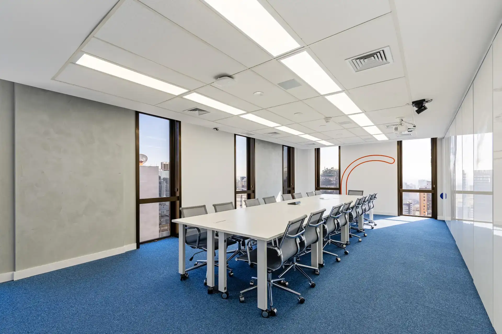 Sala de reunião ampla planejada por escritório Custódio arquitetura, com mesa longa, iluminação homogênea e comunicação visual em laranja.