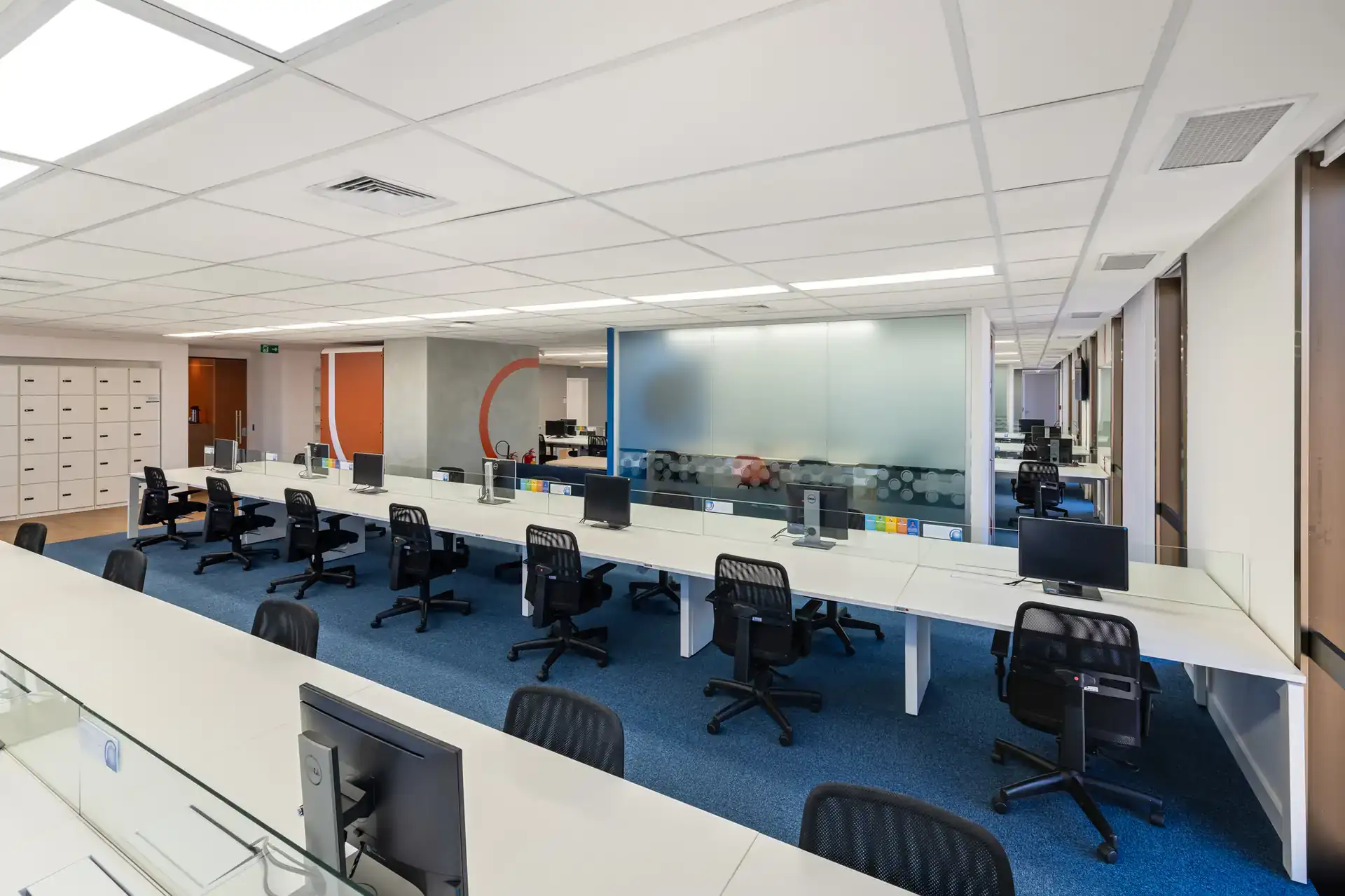 Área operacional planejada em reforma de escritório da Recovery, com bancadas contínuas, divisórias de vidro e estações ergonômicas. Tudo isso pensado em projeto de arquitetura e obra corporativa.