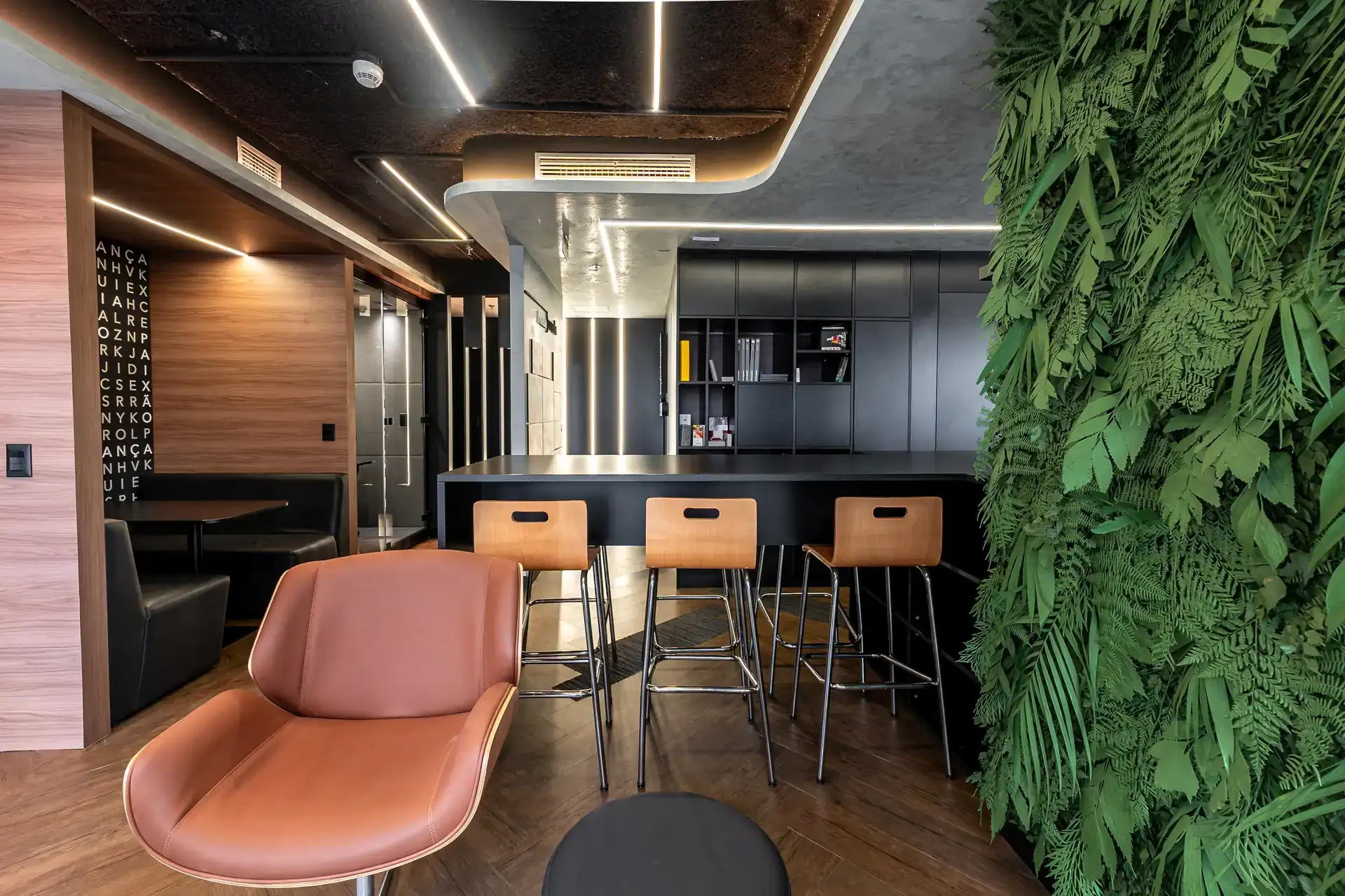 Área de café e bar do escritório da Custódio SP, com bancada preta, vegetação vertical e mobiliário aconchegante, mostrando solução de projeto de arquitetura corporativa humanizada.