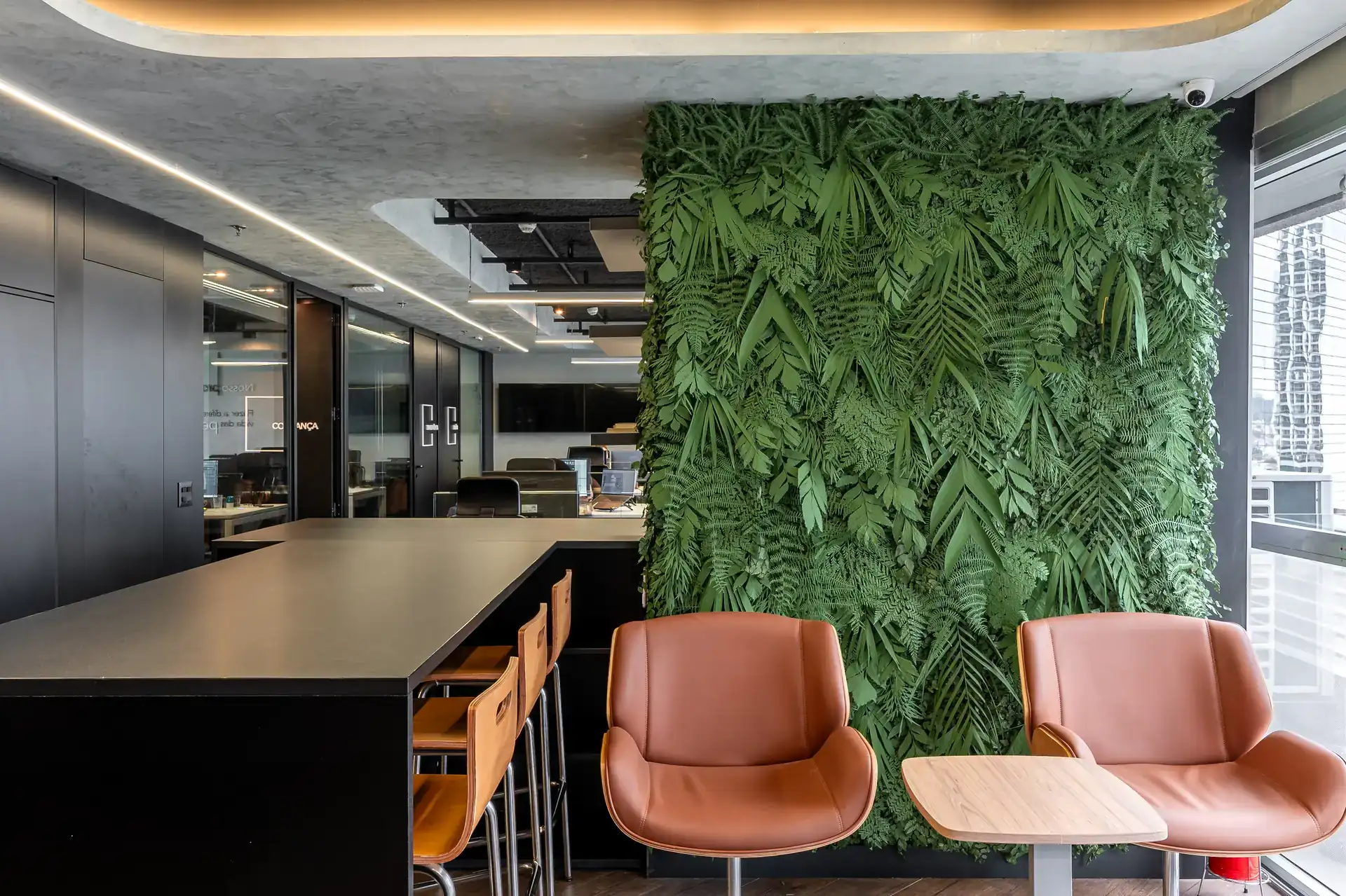 Lounge com poltronas de couro e parede verde em destaque, demonstrando elementos de reforma de escritório voltada ao bem estar e ao design biofílico.