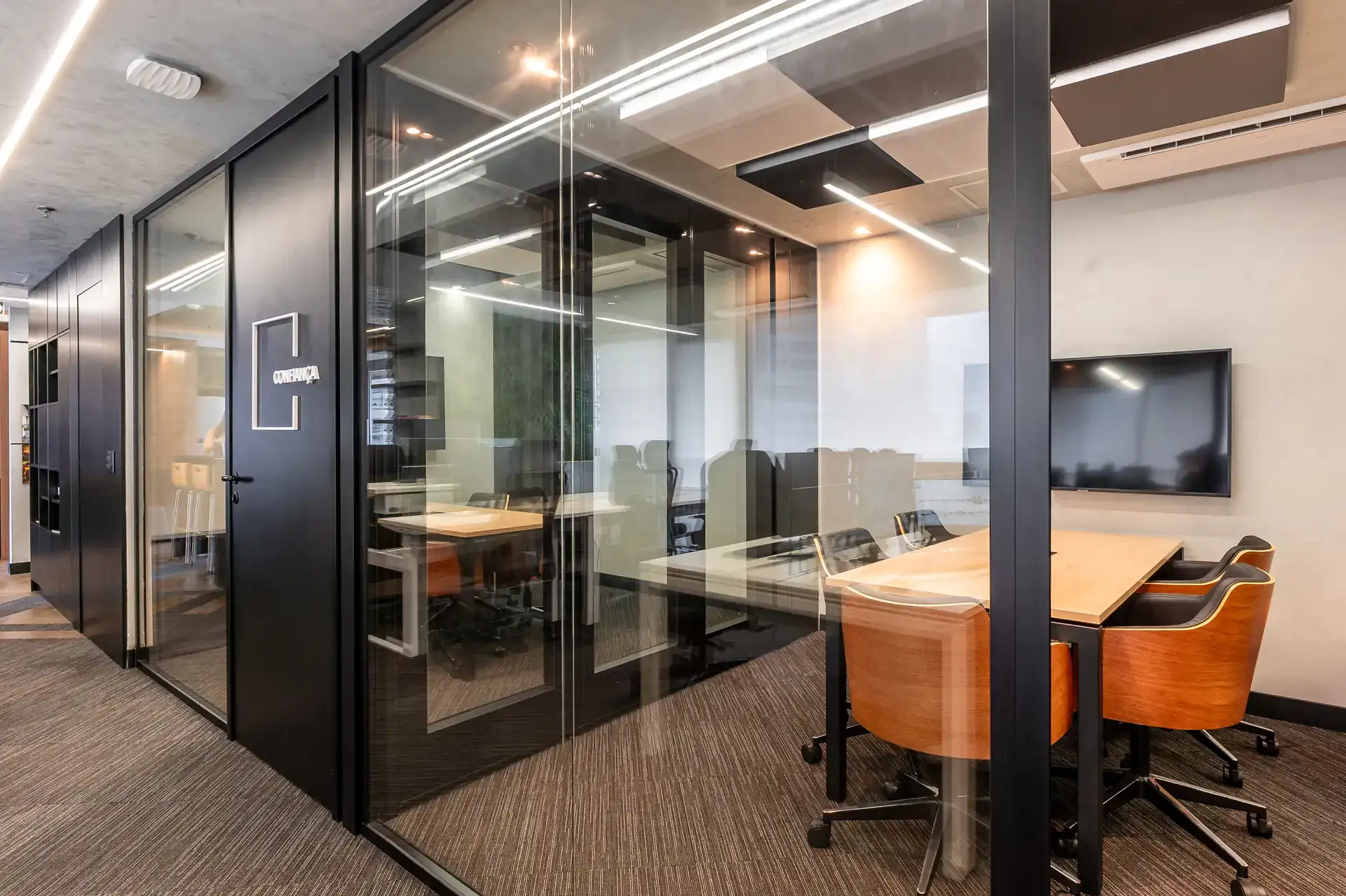 Sequência de salas envidraçadas com linhas pretas e iluminação embutida, representando soluções de projeto de arquitetura que priorizam transparência e acústica na reforma do escritório.