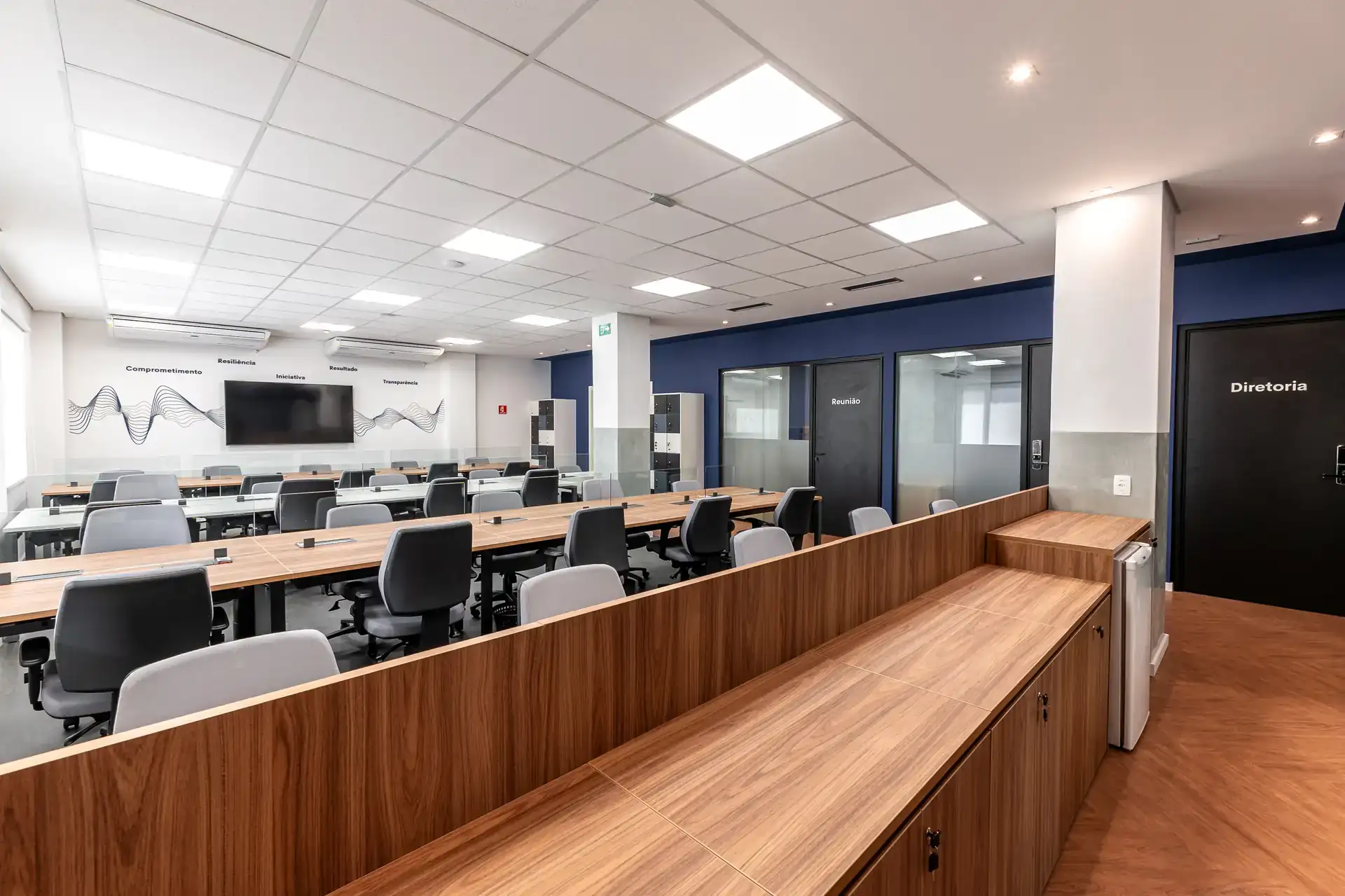 Estações de trabalho com tampo em madeira e armário lateral, compondo reforma de escritório que integra operação, diretoria e salas de reunião do escritório da LAM Medical.