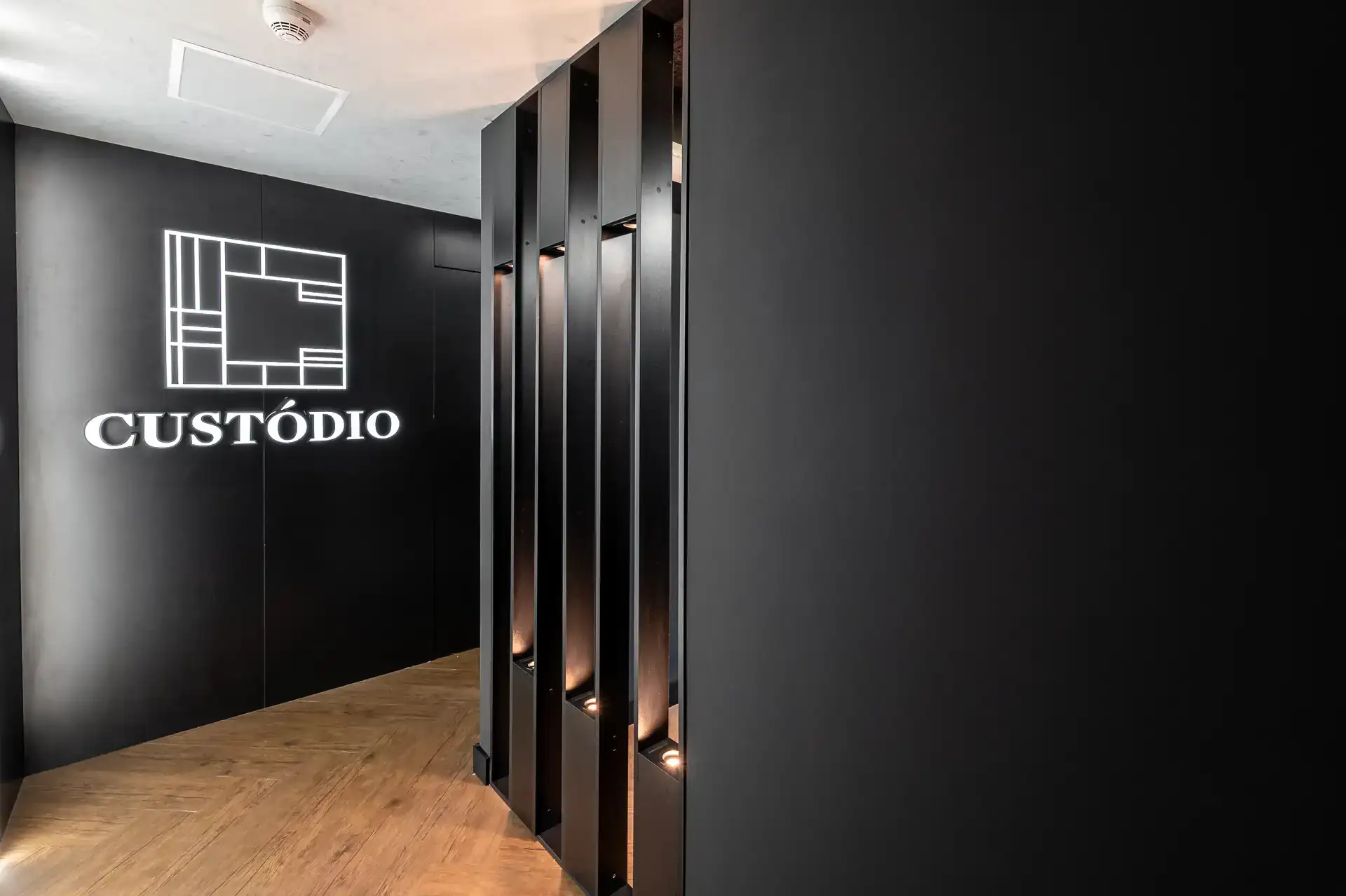 Hall de entrada do escritório da Custódio em SP, com painel preto iluminado e acabamento sofisticado, representando o início da experiência de um projeto de arquitetura de uma reforma corporativa.