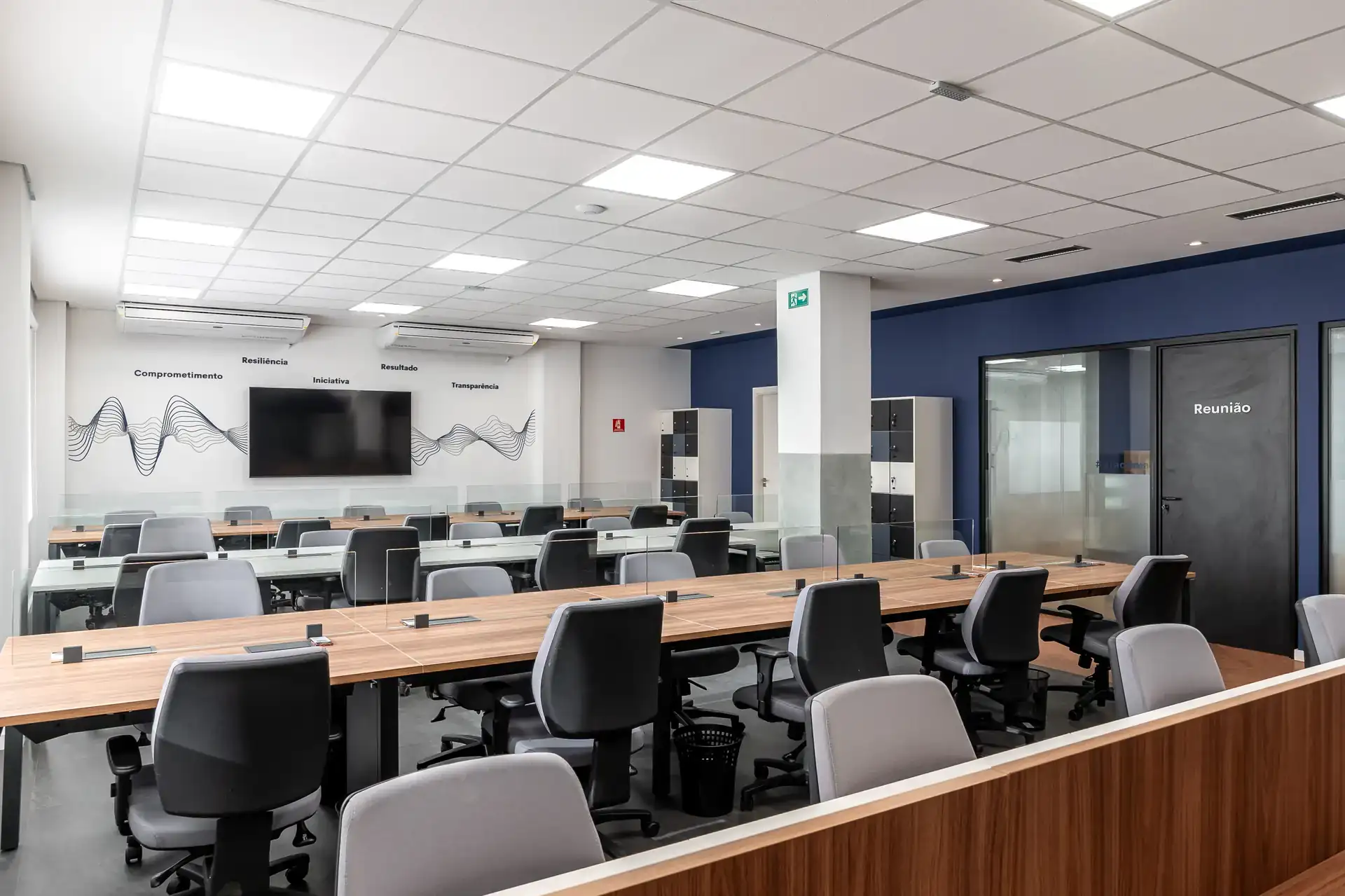 Open space do escritório da LAM Medical em vista diagonal, com mesas compartilhadas, cadeiras ergonômicas e parede azul, parte de obra e reforma corporativa assinada pela Custódio Arquitetura.