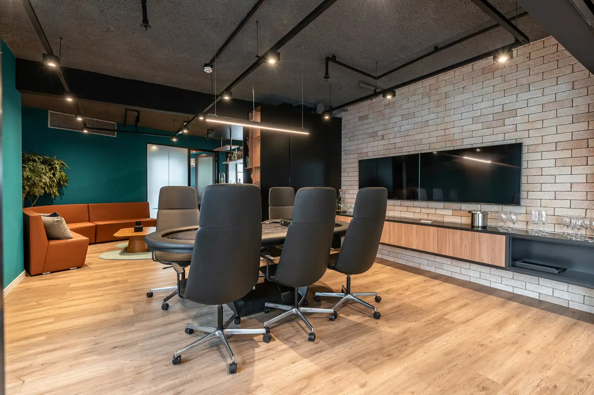 Ambiente integrado com sala de reunião e lounge, destacando madeira, iluminação pontual e composição moderna em obra corporativa do escritório da MHM.