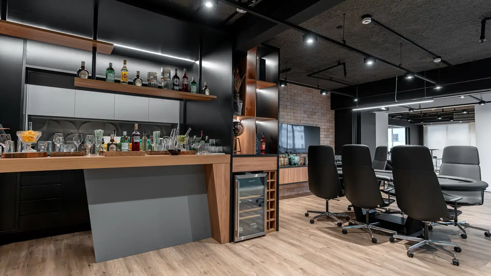 Bar corporativo com prateleiras iluminadas, bebidas expostas e área integrada à sala de reuniões, parte do projeto de arquitetura do escritório da MHM.