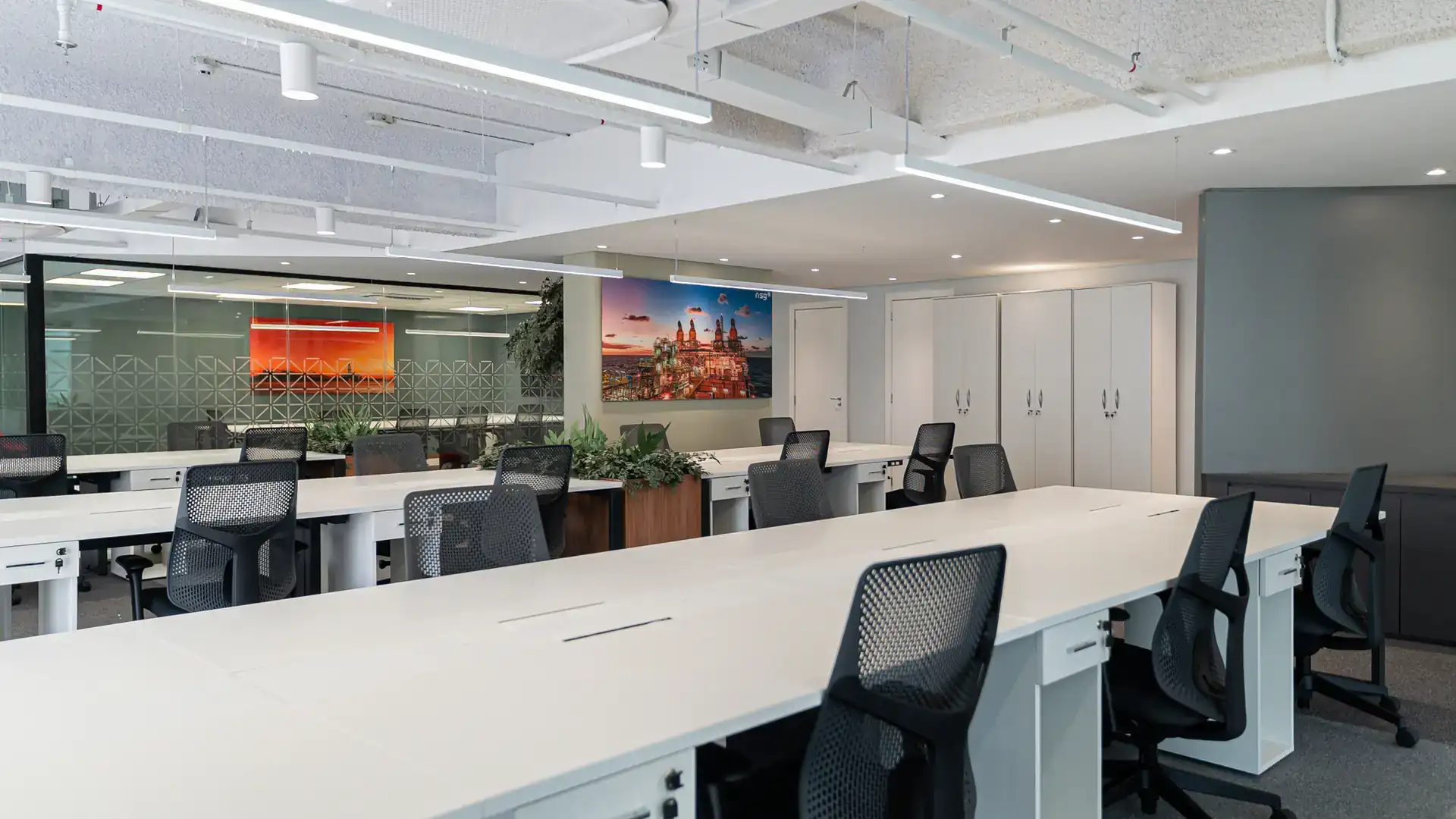 Área colaborativa ampla com estações de trabalho brancas, cadeiras pretas e iluminação natural, planejada no projeto de arquitetura e executada na obra corporativa do escritório da NSG.