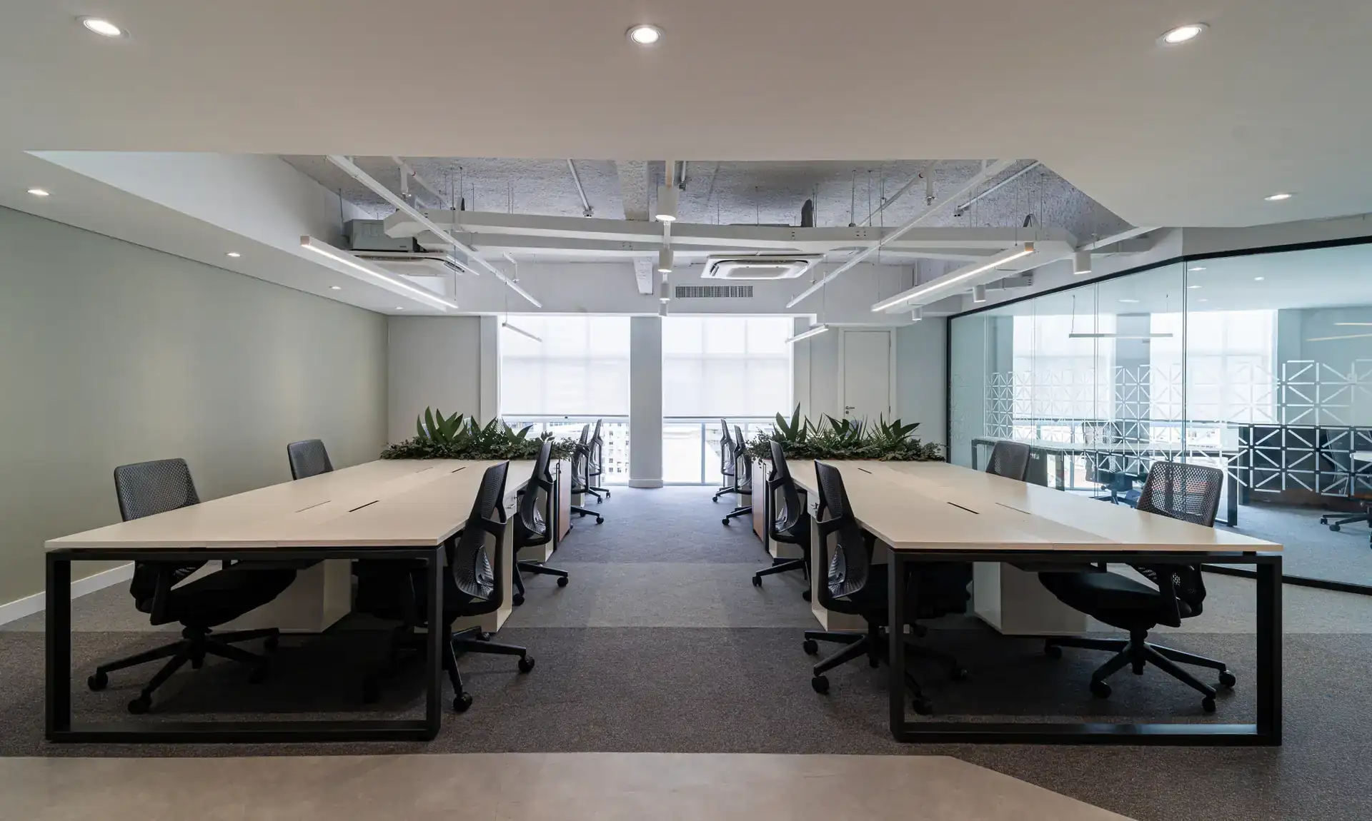 Estações de trabalho amplas com iluminação natural, vegetação central e layout funcional desenvolvido em projeto de arquitetura corporativa.