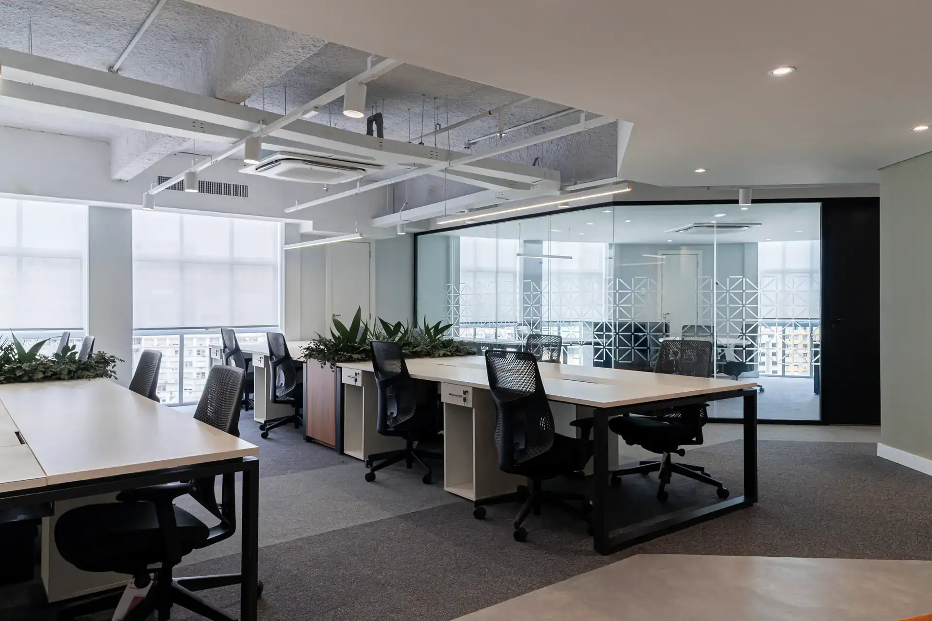 Layout colaborativo em escritório no Rio de Janeiro, com mesas, cadeiras ergonômicas e divisórias envidraçadas após reforma corporativa completa.