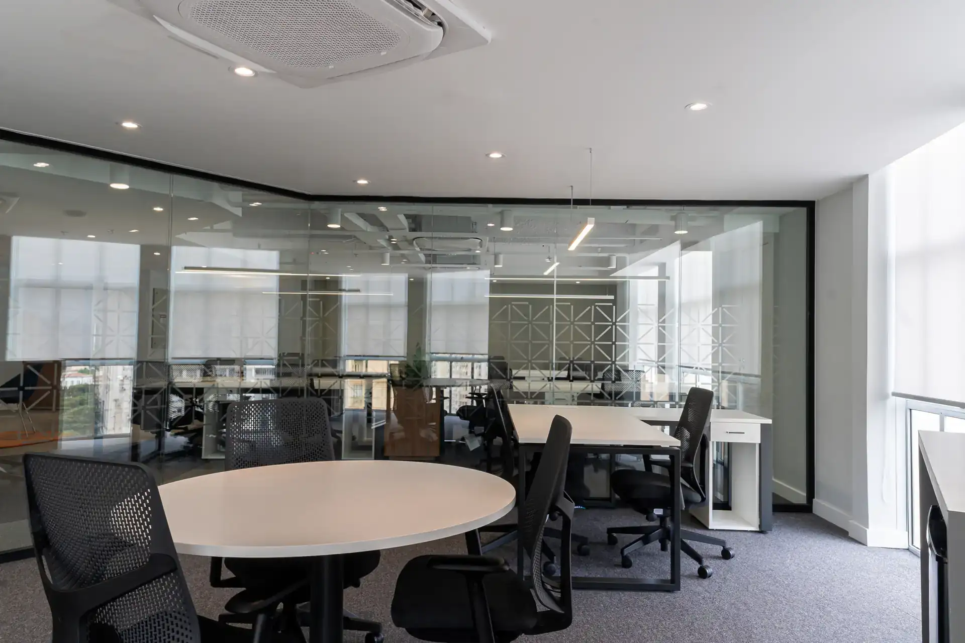 Sala de diretoria com mesa redonda, cadeiras ergonômicas e divisória de vidro projetado para estimular reuniões rápidas no escritório da NSG, após reforma corporativa completa.