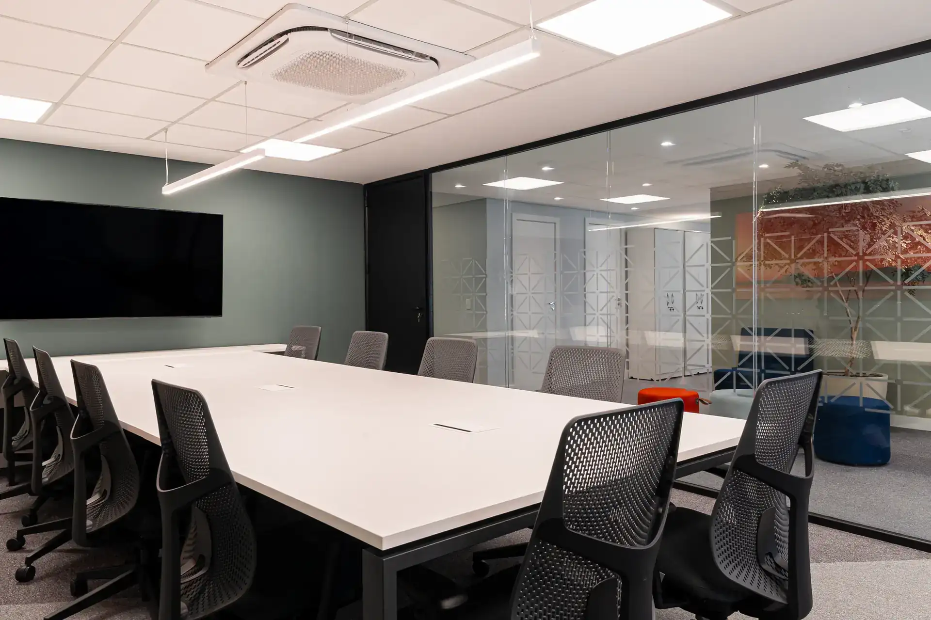 Sala de reunião executiva com mesa branca, cadeiras ergonômicas e divisória de vidro, parte da obra corporativa do escritório da NSG.