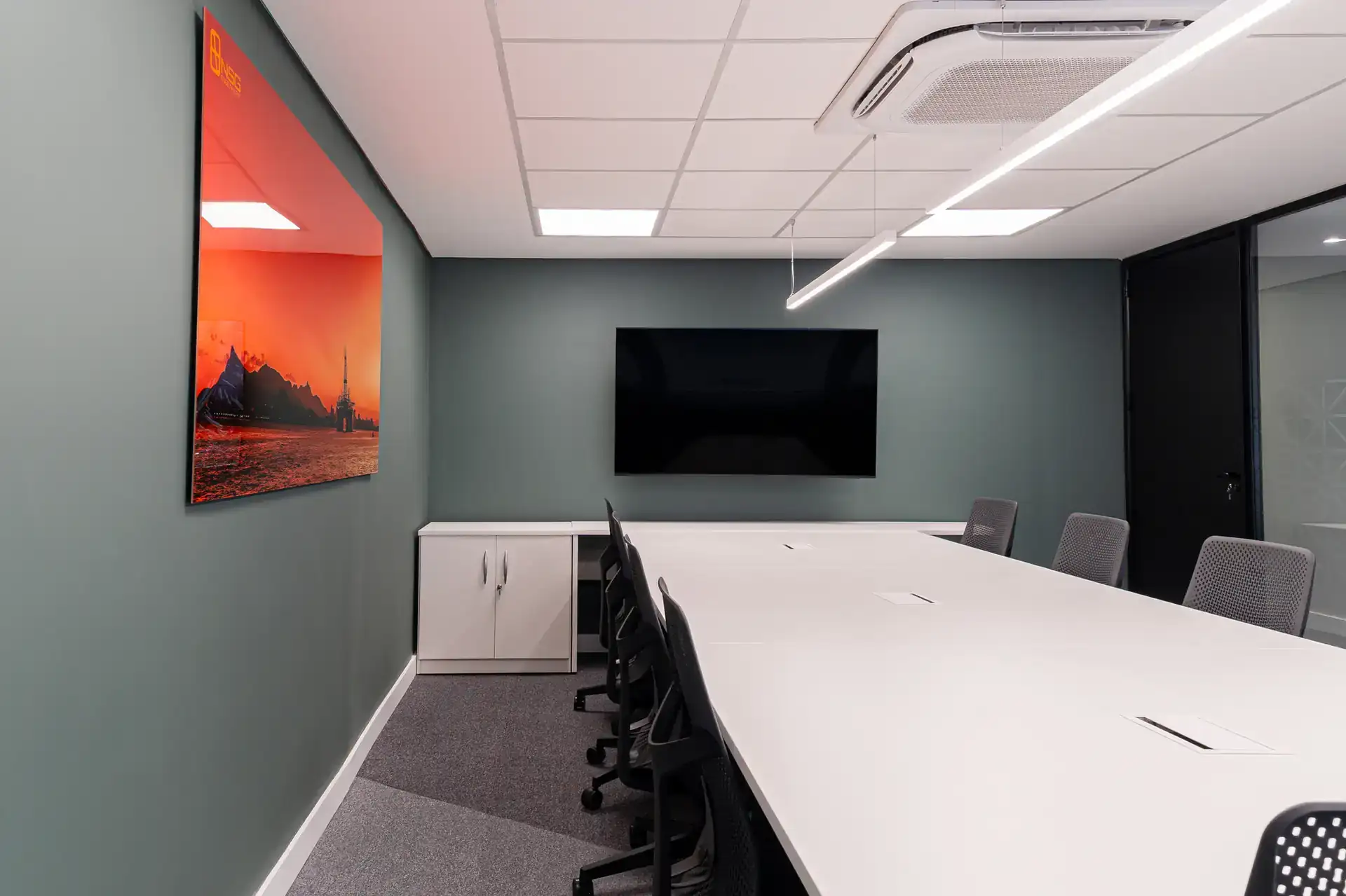 Sala de reunião do escritório da NSG, após reforma corporativa completa, com parede verde, tela de apresentação e iluminação linear em ambiente planejado para uso corporativo. Resultado de um projeto de arquitetura e obra no escritório.