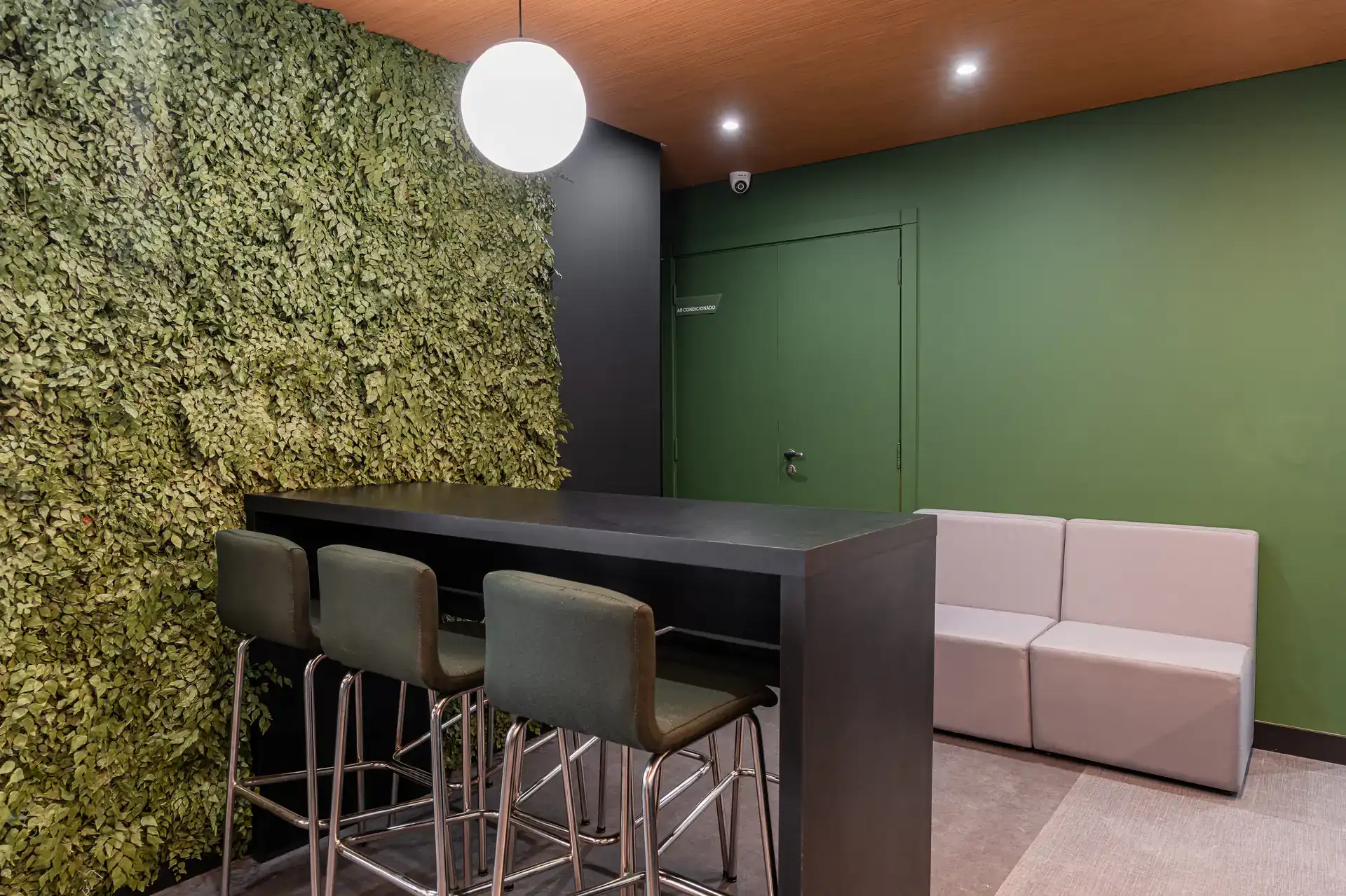 Área de convivência com bancada alta e parede verde natural, criada na reforma corporativa do escritório da Oplium.