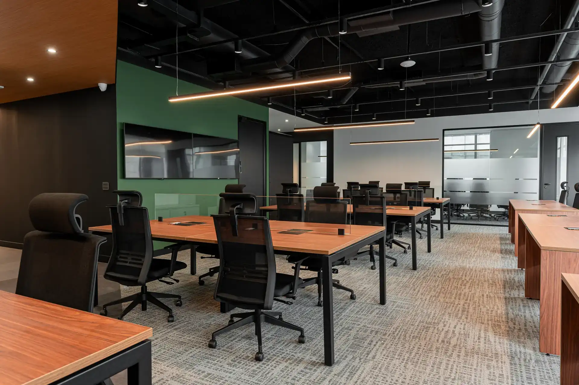 Open space do escritório da Oplium com mesas em madeira, cadeiras ergonômicas e televisores integrados ao layout do projeto de arquitetura corporativa.