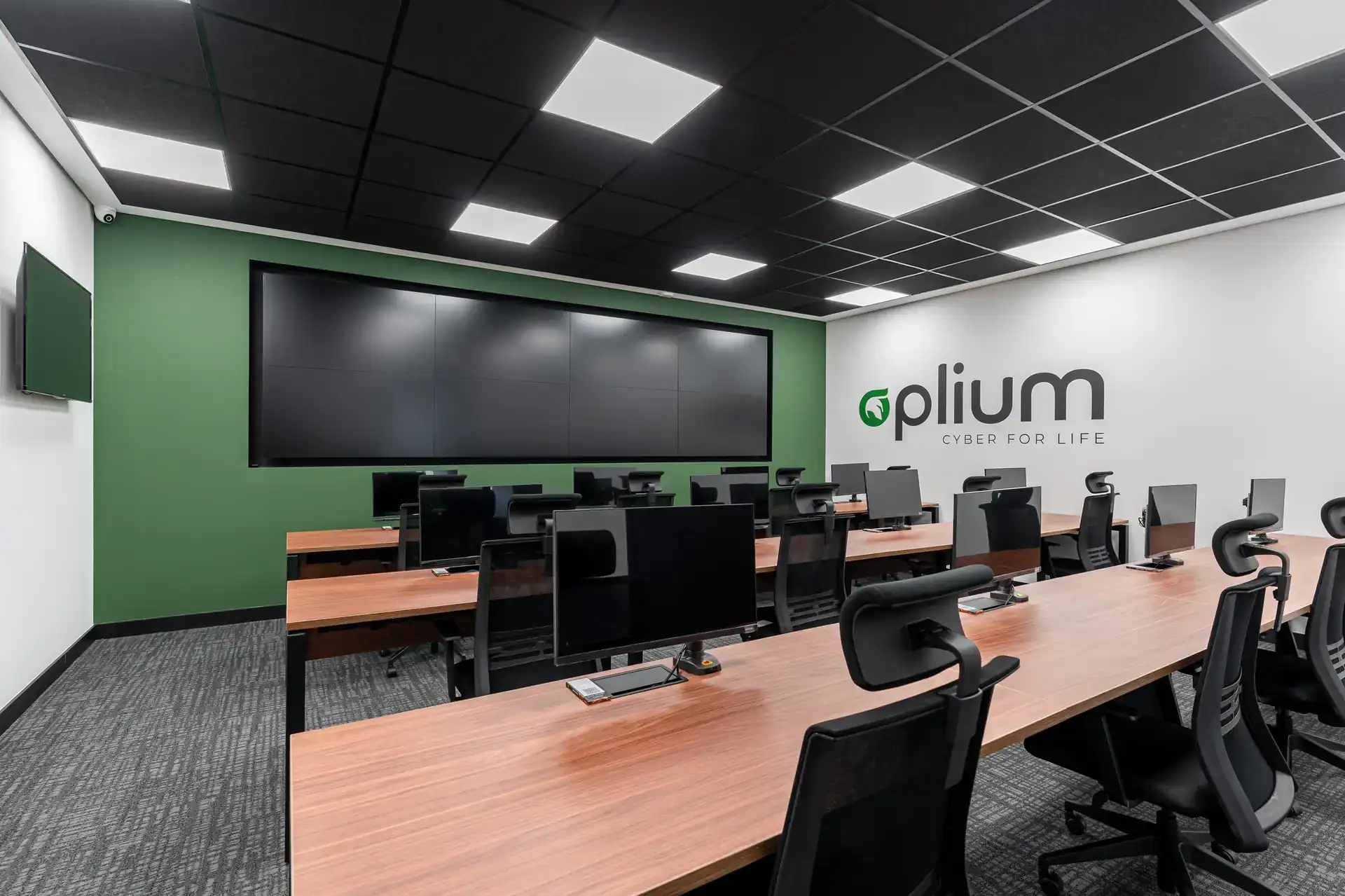 Espaço de operações com videowall e mesas lineares em madeira, parte do projeto de arquitetura desenvolvido para o escritório da Oplium, executado por meio de uma obra corporativa.